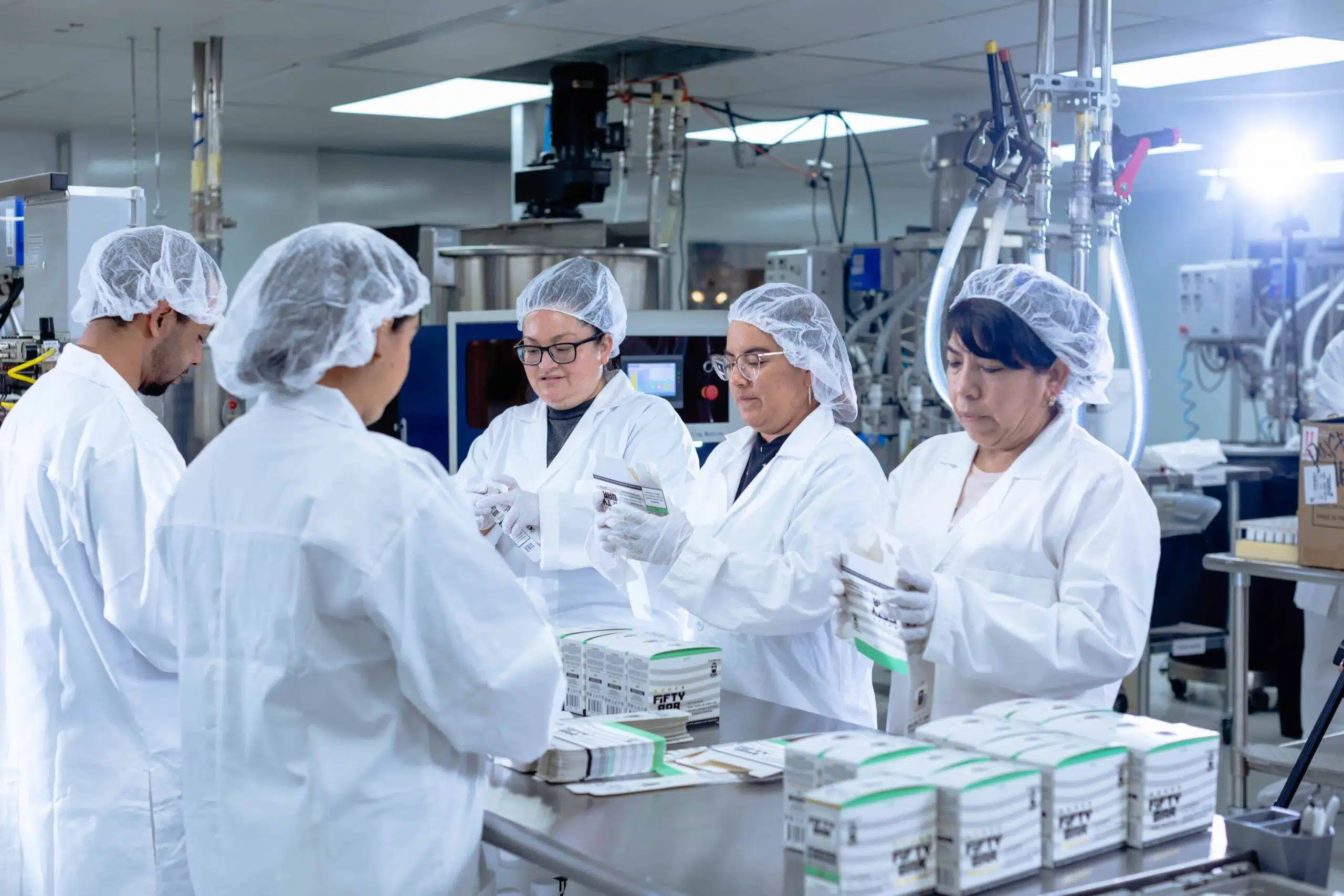 Fifty Bar Vape manufacturing facility — workers in white lab coats packaging devices